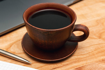 Work wooden office table with coffee cup, laptop, notepad and pen