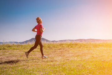 young woman jogging on sunny day at summer mountain