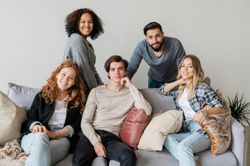 Group of happy young intercultural friends in casualwear relaxing on soft couch