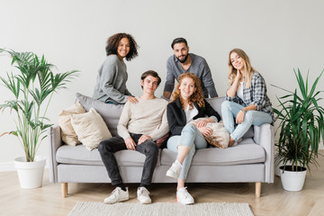 Joyful intercultural teenagers in casualwear relaxing on sofa together