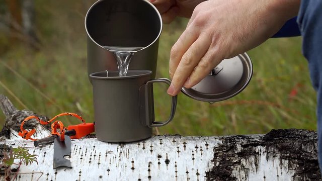 Close-up video of a tourist making tea. Titanium cup on a fallen tree.