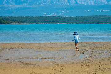 5 years old boy exploring the beach at low tide with a scenic landscape as background - Soline, Krk, Croatia