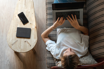 Woman with a laptop laying on a sofa. Study and work online, freelance. Self employed woman, girl...