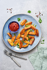 Fried potatoes with tomato sauce, spices and greens in a plate on a gray background. Top view, flat lay