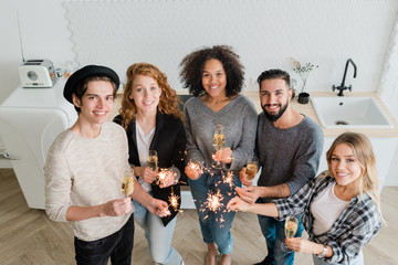 Young cheerful friends with flutes of champagne and sparkling bengal lights