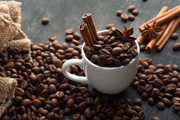 Weiße Tasse voller Kaffeebohnen Zimtbeutel verschüttet Kaffeesterne Anis Sternanis auf dunklem Hintergrund