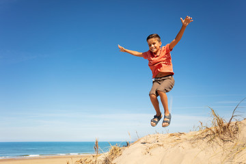 Obraz premium Cute boy jump on the sand dune beach with hands up