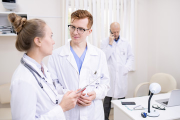 Two young colleagues in whitecoats discussing medical stuff in clinics