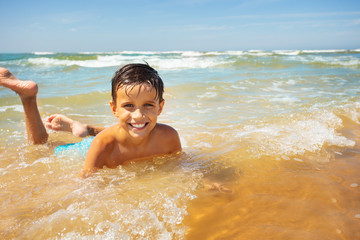 Happy boy lay in the sea waves smiling on a beach