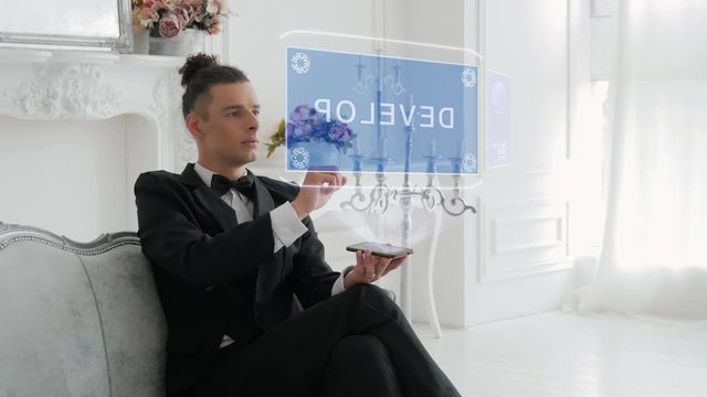 Guy businessman activates conceptual HUD hologram on smartphone with text Develop. Young man in a white shirt and a jacket with a holographic screen on a background of the luxury room