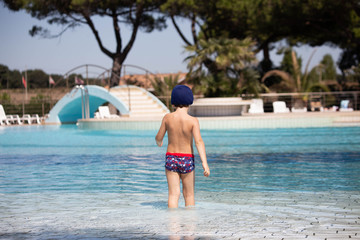 BAMBINO VISTO DI SPALLE CHE  ENTRA IN ACQUA IN UNA PISCINA ALL'APERTO