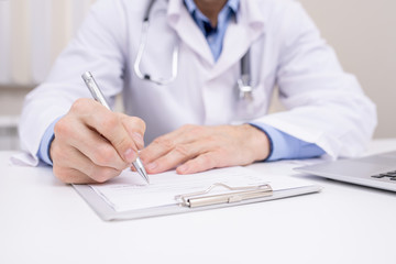 Hand of professional clinician with pen over clipboard with medical document