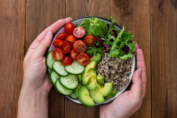 Healthy food. Womans hand holding budha bowl with quinoa, avocado, cucumber, salad, tomatoe, olive oil. Clean eating, diet food. Lose weight.