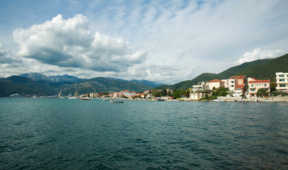 Fototapeta na wymiar Bay in seaside town with boats, houses in green mountains on blue sky,.Tivat, Montenegro