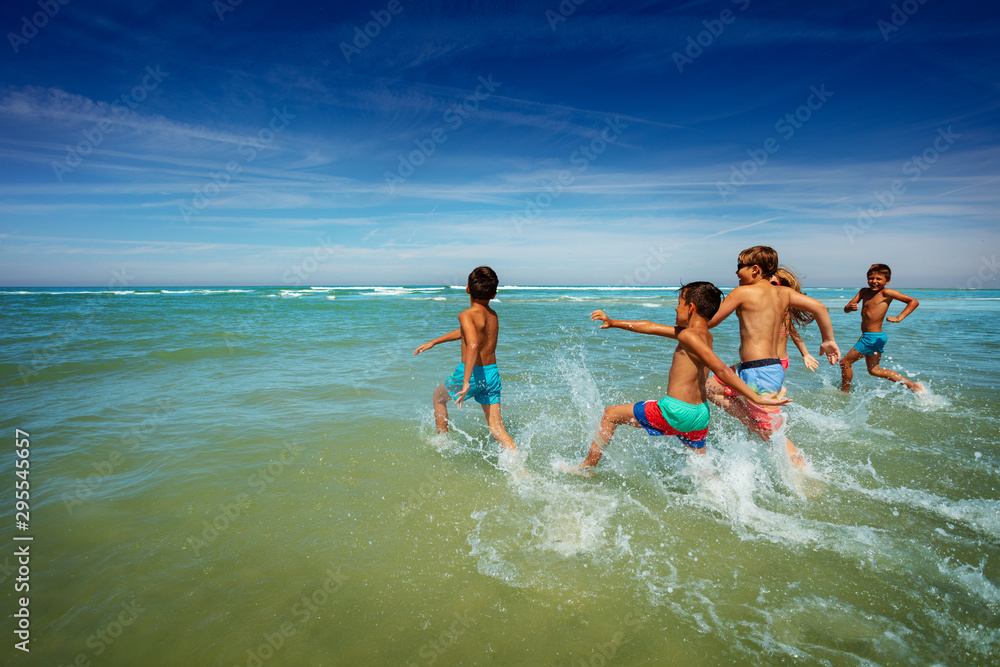 Wall mural many boys and girls run to ocean waves on a beach