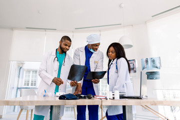 Fototapeta premium Healthcare, medical: Group of three young African doctors, two men and woman, discuss and looking x-ray in a clinic or hospital