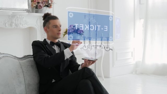 Guy businessman activates conceptual HUD hologram on smartphone with text E-ticket. Young man in a white shirt and a jacket with a holographic screen on a background of the luxury room