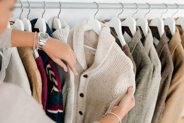 Hands of young woman holding white knitted cardigan while choosing new clothes