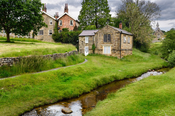 Hutton Beck flowing through Hutton-le-Hole village with stone houses on the village green North York Moors National Park England