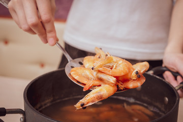 female hand takes out shrimp from a pan