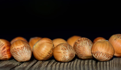 Several brown nuts with shell lie side by side against dark background with open space in autumn