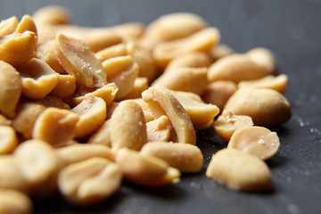 Roasted peeled peanuts closeup, salty beer snack scattered on black stone background