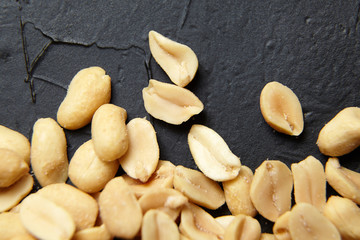 Roasted peeled peanuts closeup, salty beer snack scattered on black stone background