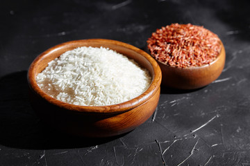 Red and white rice in a wooden bowls on black stone table. Dry uncooked grains. Ingredient for cooking various dishes