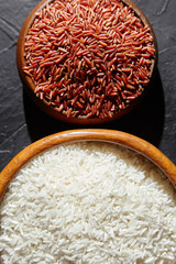 Red and white rice in a wooden bowls on black stone table, top view. Dry uncooked grains. Ingredient for cooking various dishes
