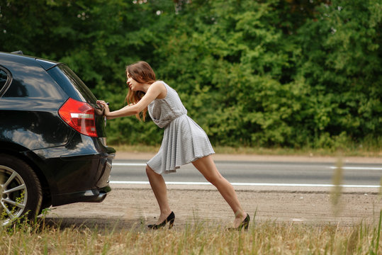 Woman pushing broken car on road, breakdown