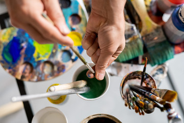 Fototapeta premium Hands of painter holding paintbrush over glass of water while cleaning it