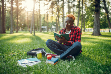 Fototapeta premium Black student in glasses reading book on the grass