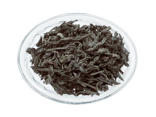 Leaves of black tea in glass oval bowl closeup isolated on white background top view                              