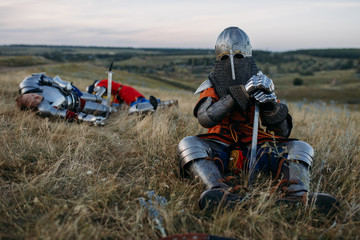 Medieval knight in armor sitting on the ground - obrazy, fototapety, plakaty