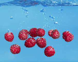 Fresh ripe raspberries falling in water on grey background