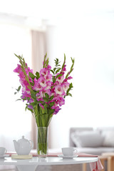 Vase with beautiful pink gladiolus flowers on wooden table in living room