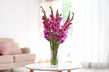 Vase with beautiful pink gladiolus flowers on wooden table in living room