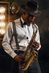 Plakat Black jazzman in hat plays the saxophone on stage