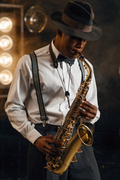 Black jazzman in hat plays the saxophone on stage