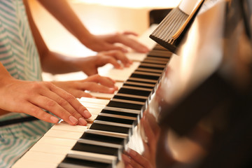 Fototapeta premium Young woman teaching little girl to play piano indoors, closeup