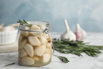 Composition with jar of pickled garlic on marble table against blue background. Space for text