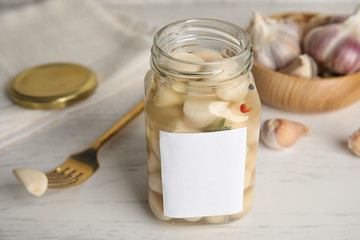 Composition with jar of pickled garlic on white wooden table