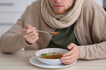Sick young man eating soup to cure flu at table indoors