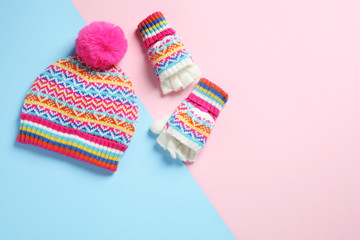 Warm knitted hat and mittens on color background, flat lay. Space for text
