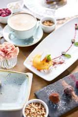 Yellow mousse-cake. Breakfast in the cafe, morning coffee. Cappuccino and lots of desserts on the table. French dessert, blueberry, mint and a piece of meringue on a white plate. Restaurant menu