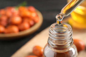 Dripping jojoba oil from pipette into bottle on blurred background, closeup. Space for text