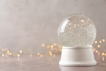 Snow globe on marble table against festive lights, space for text. Christmas season