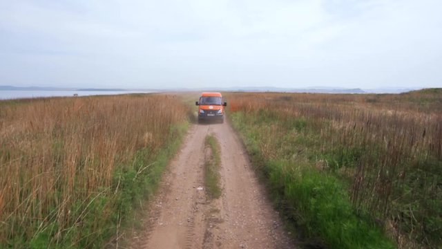 Summer, 2019 - Primorsky Krai, Russia - Orange expedition minibus Sable driving along a dusty dirt road among green fields.