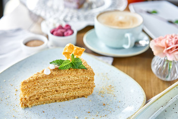 Honey sponge cake decorated with meringue and mint leaves.. Breakfast in the cafe, morning coffee. Cappuccino and lots of desserts on the table.
