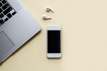 flat lay, office desktop, laptop, smartphone, phone, wireless bluetooth headphones on light yellow...